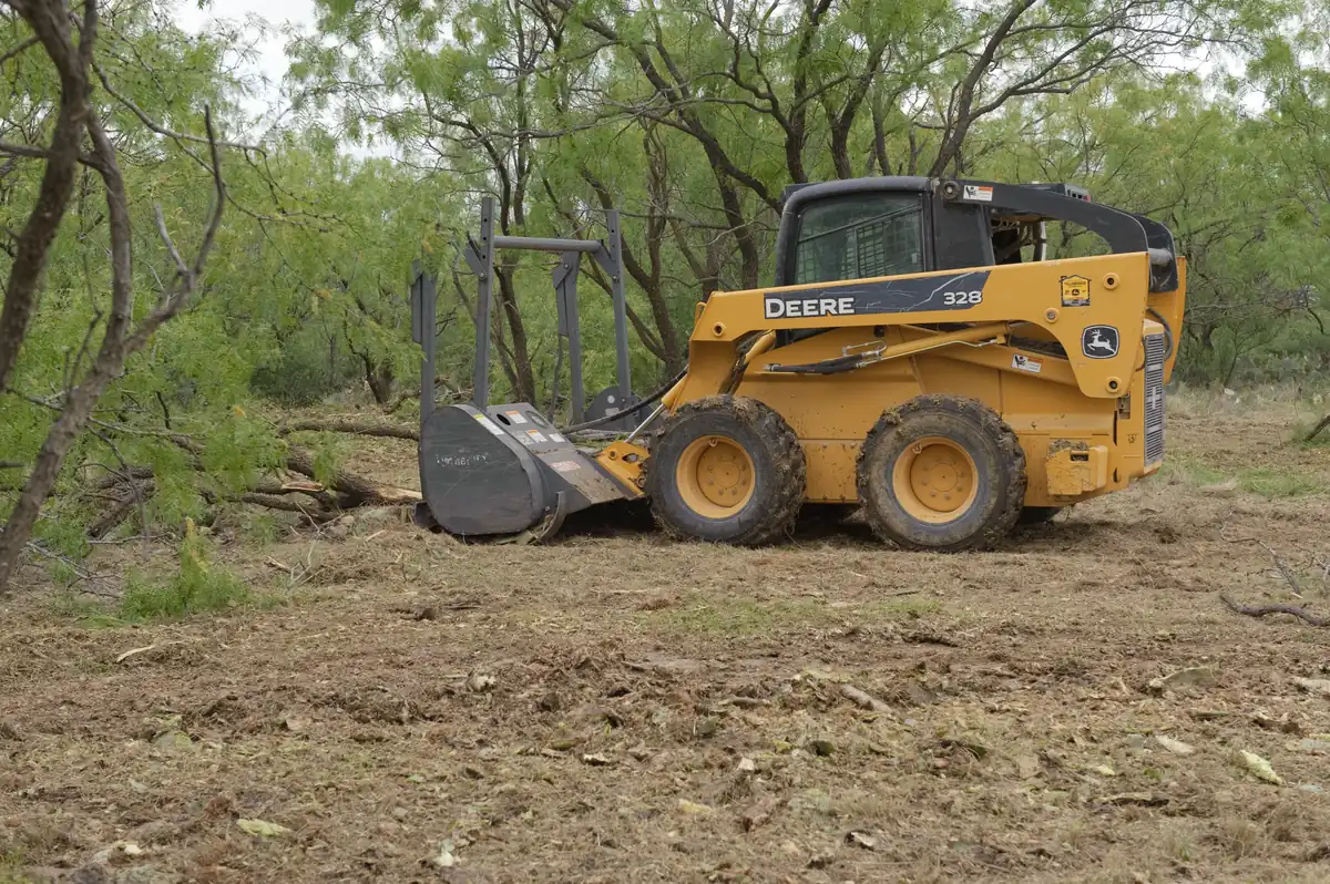 Skid steer with a clearing attachment pushing through dense brush and small trees